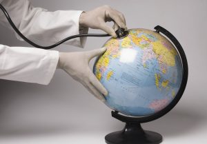Close-up of a person's hands examining a globe with a stethoscope to show climate change
