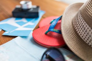 summer vacation, tourism and objects concept - close up of travel map, airplane tickets, flip-flops and hat to illustrate buying a second home